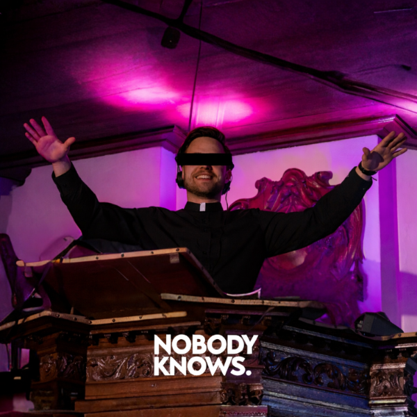 Person with arms outstretched in a dimly lit room with purple lighting, wearing a blindfold with 'Nobody Knows' text.